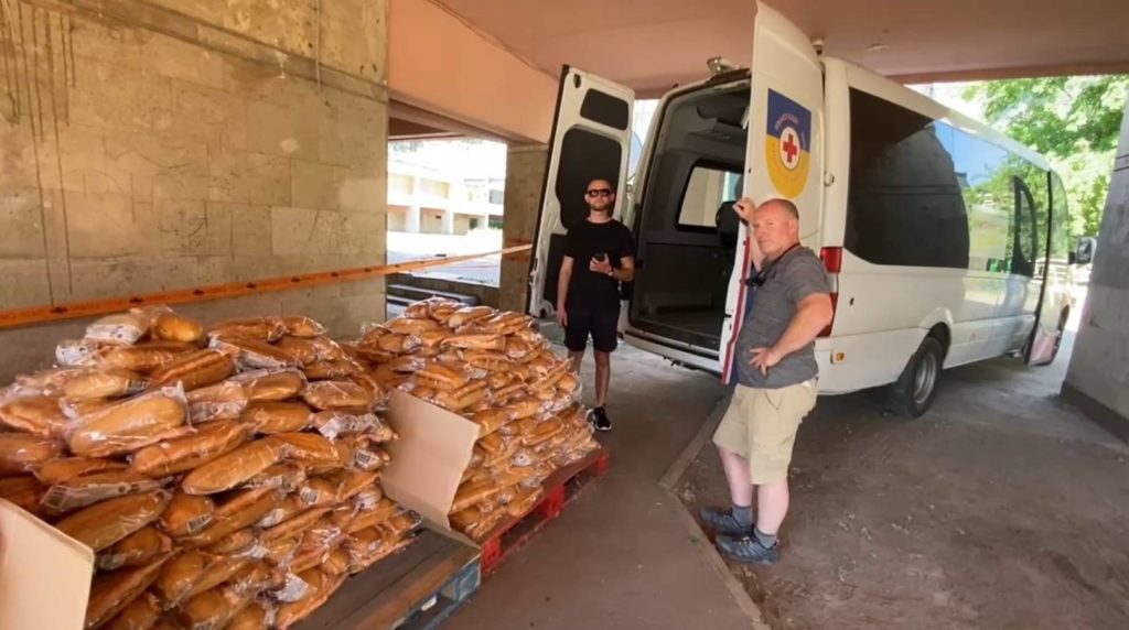 2 men with a bunch of bread in front of a van